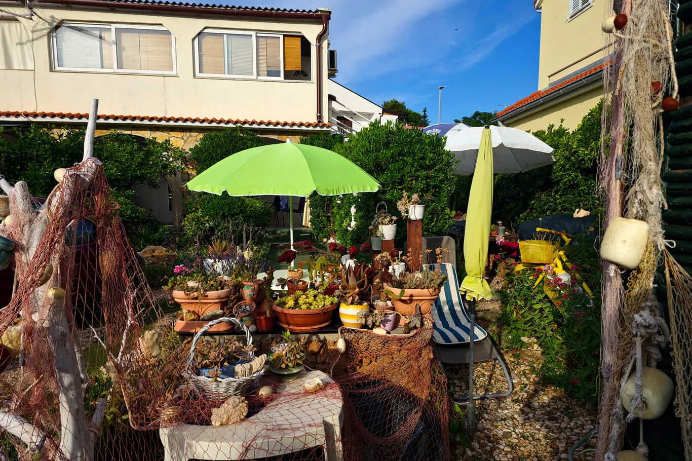 Two umbrellas over the Bobinac garden dining area at golden hour, with terracotta pots and fishing nets on the walls