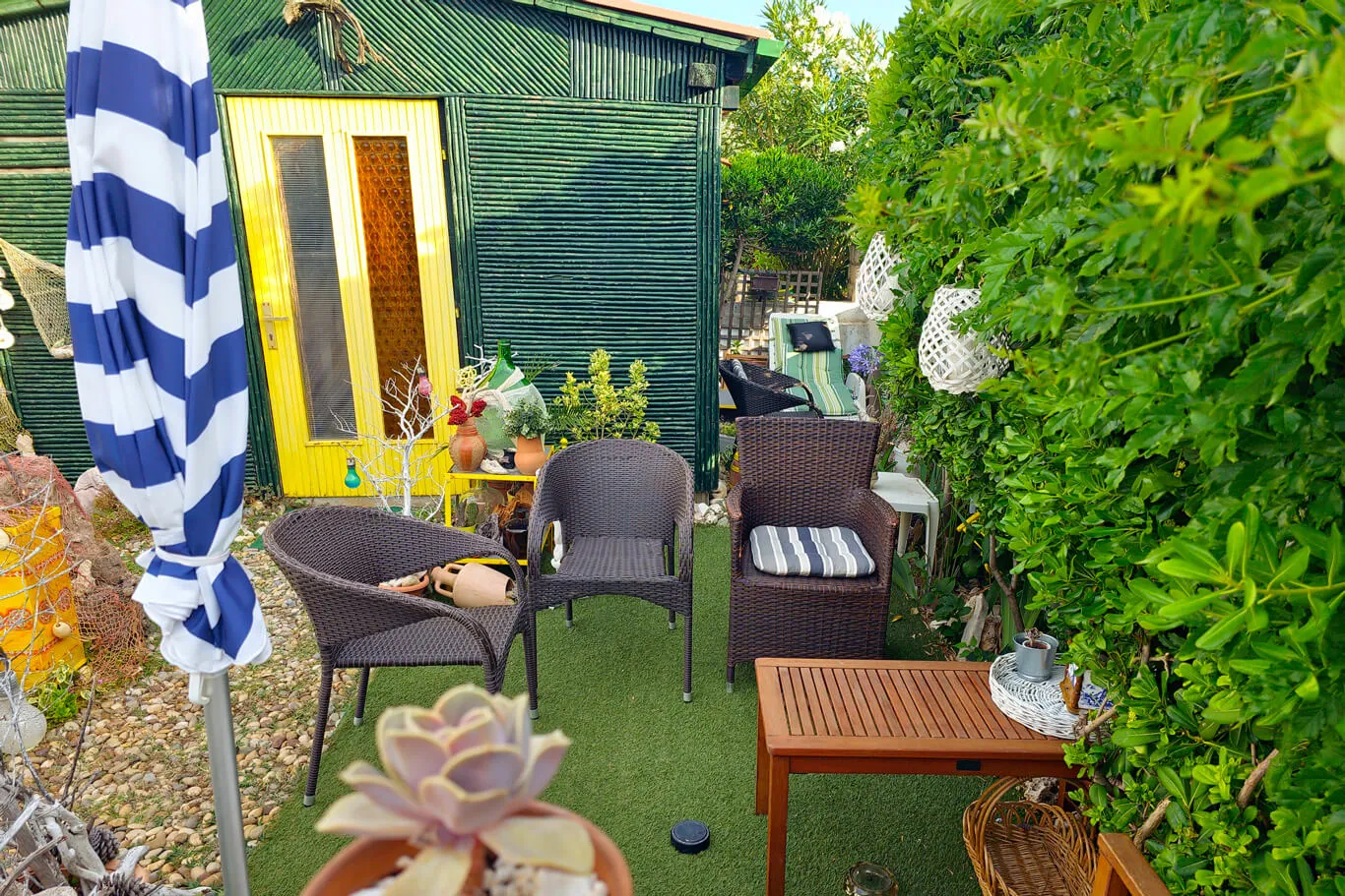 The green corrugated chalet with its bright yellow door, wicker lounge seating and striped umbrella